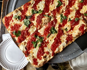 rectangular grandma pizza with sauce on top and basil