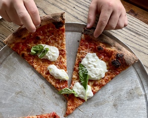 two people reach for slices of pizza topped with burrata