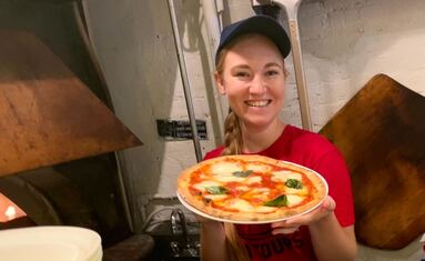 a woman holds a pizza in front of a pizza oven