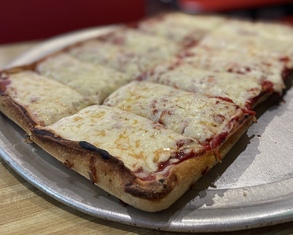 a square pizza covered with cheese sitting on a round aluminum tray