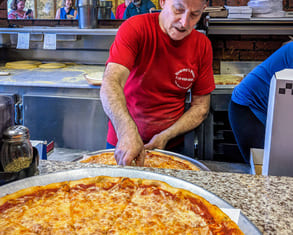 a man in a red shirt slices a perfect new york pizzza