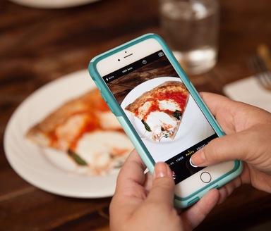 a smart phone taking a picture of a slice of Neapolitan pizza