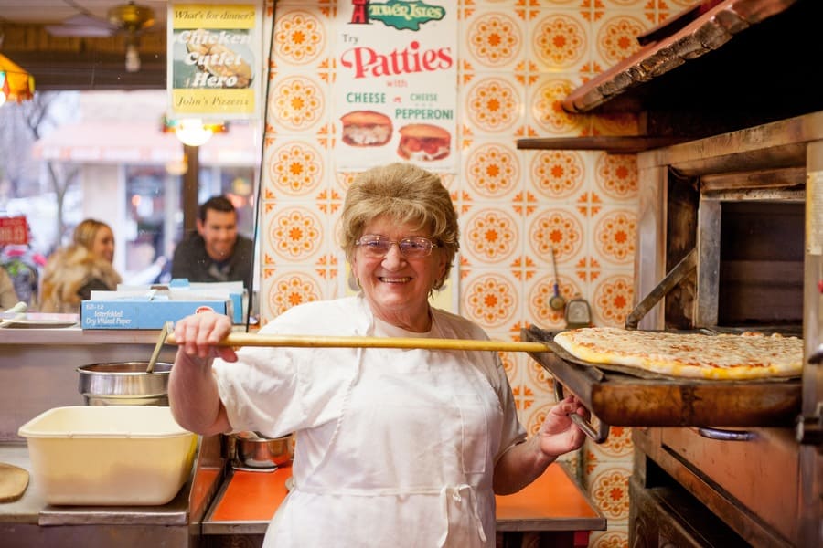 a woman holding a pizza next to a pizza oven