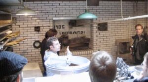 a man points to a coal fired brick oven while giving a pizza tour in new york city